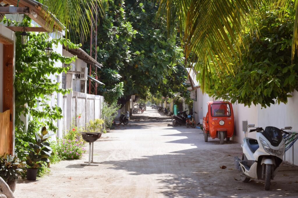Charming street in Thoddoo, Maldives, lined with lush greenery and parked motorcycles.