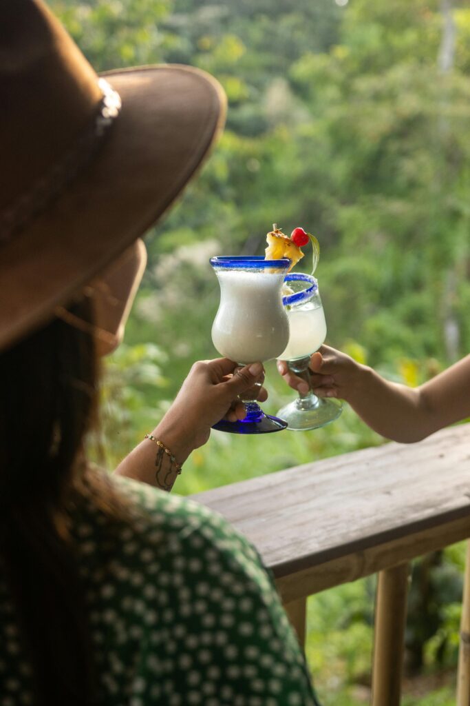 Te ayudo a organizar experiencias que realmente merece la pena vivir Enjoy a tropical toast with pina colada cocktails against a lush outdoor backdrop. Perfect for party vibes.