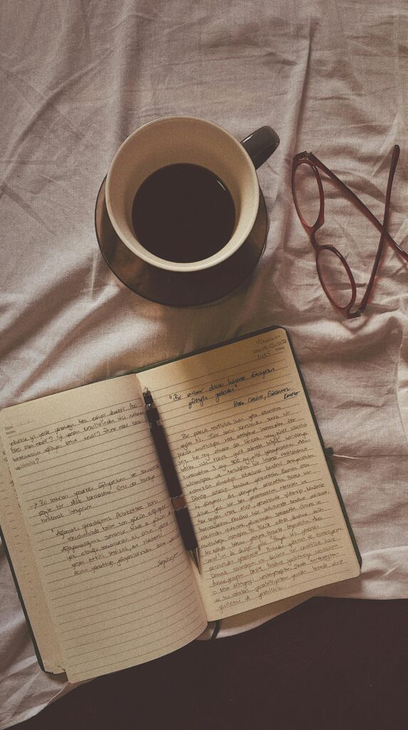 Te ayudo a organizar experiencias que realmente merece la pena vivir Flat lay of coffee, open notebook, pen, and eyeglasses on a fabric surface.