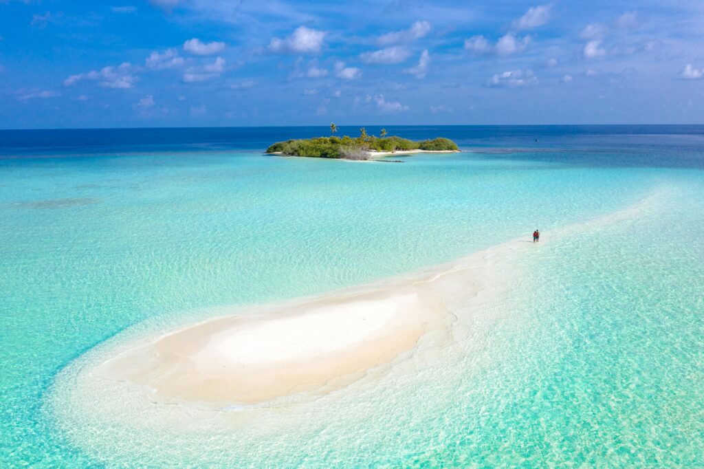 Te ayudo a organizar experiencias que realmente merece la pena vivir A breathtaking aerial view of a tranquil sandbar leading to a tropical island surrounded by azure waters.