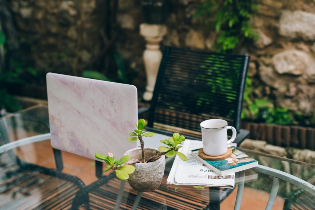 Guías & Inspiración Serene outdoor workspace setup with a laptop, coffee mug, and a small plant on a glass table.